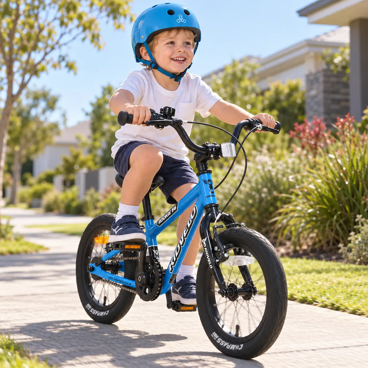 Three-year-old boy wearing a blue Triple Eight helmet and happily pedalling a blue Kidvelo Rookie 14 along an Australian suburban pathway.